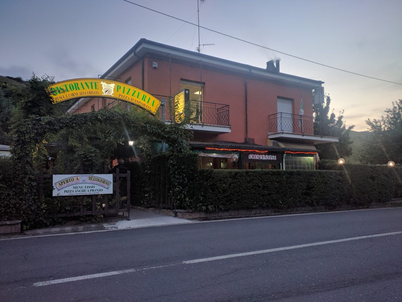 La casa gialla di Le Querce con l'insegna illuminata, all'imbrunire, lungo la Via Zena